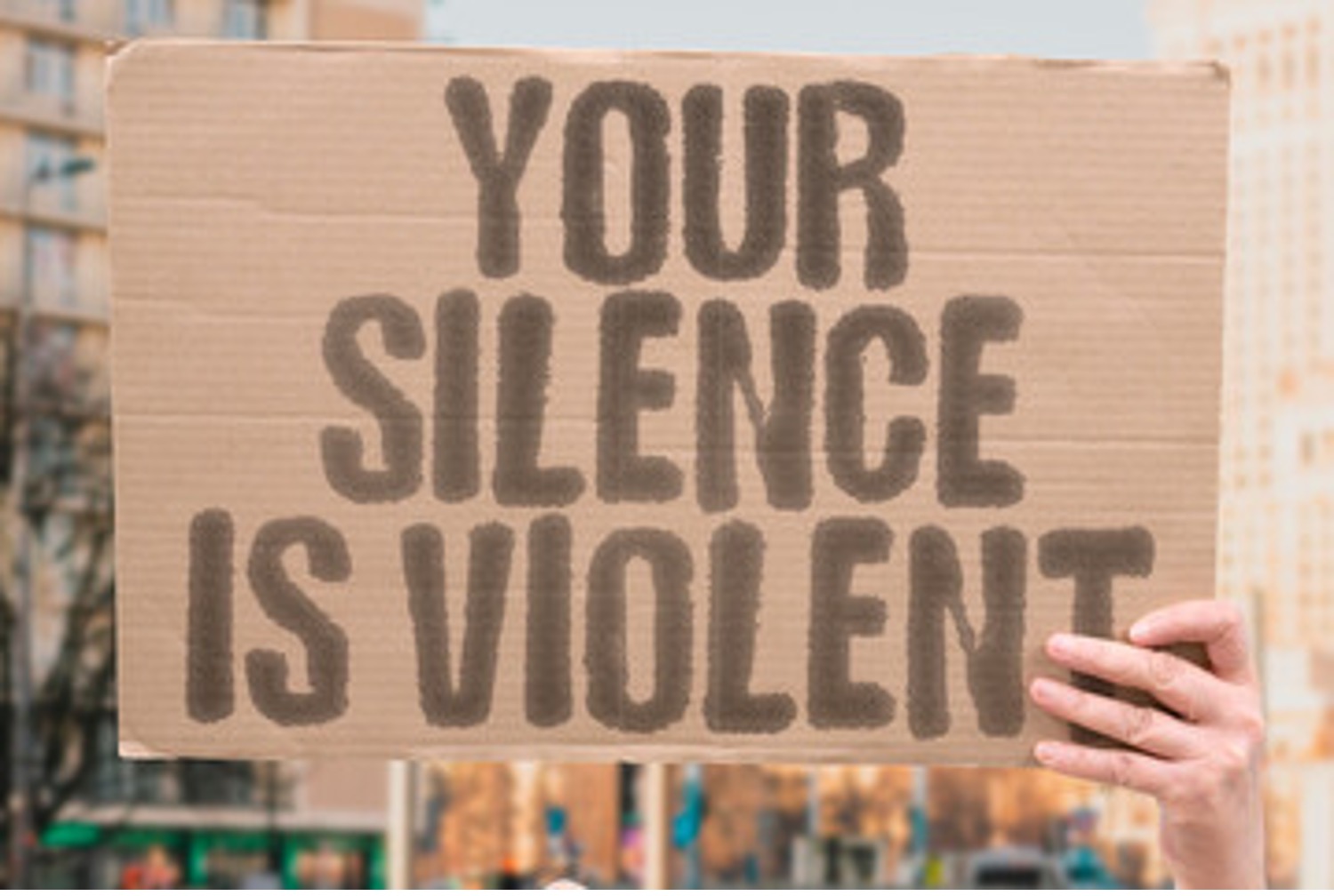 Holding cardboard sign stating Your Silence is Violent