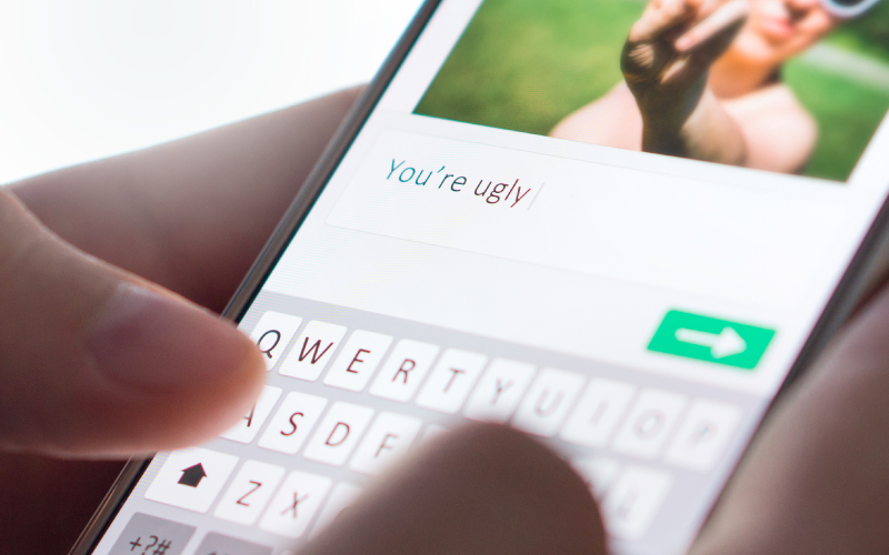 A student is typing a text message that says, 'you're ugly'