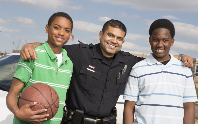 A cop and two students pose for a photo while playing basketball